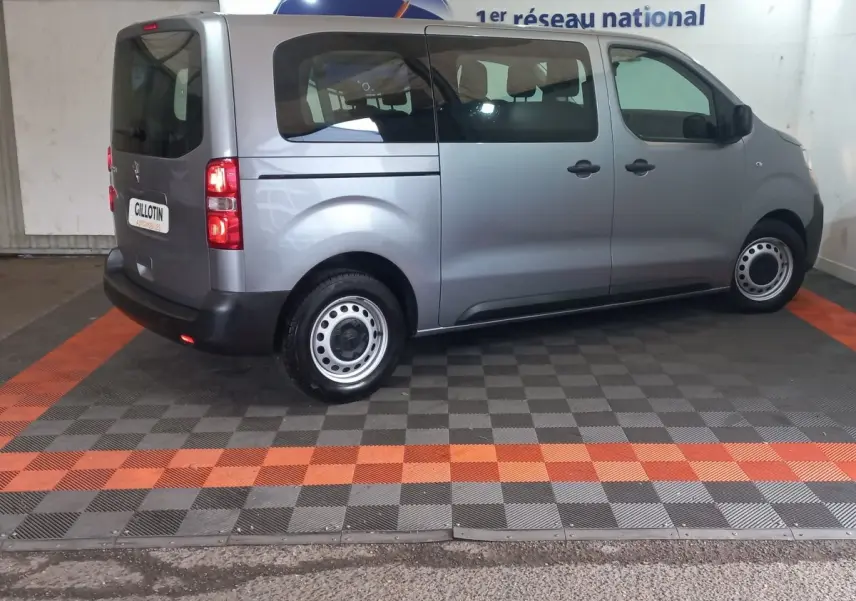 Vue latérale droite d’un Peugeot Traveller gris clair 2021 avec vitres arrière teintées et jantes acier simples.