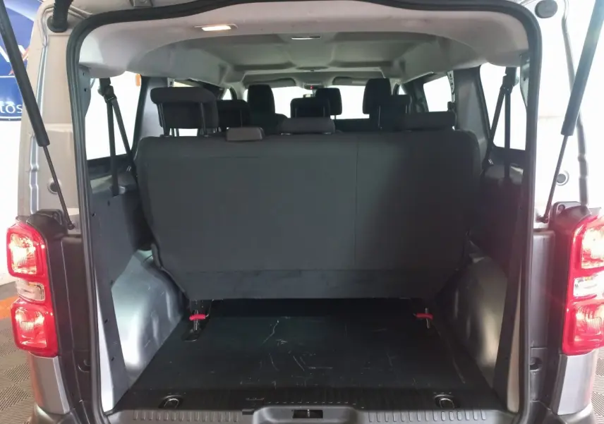Vue arrière ouverte du Peugeot Traveller gris clair montrant la troisième rangée de sièges rabattables et l'espace de coffre.
