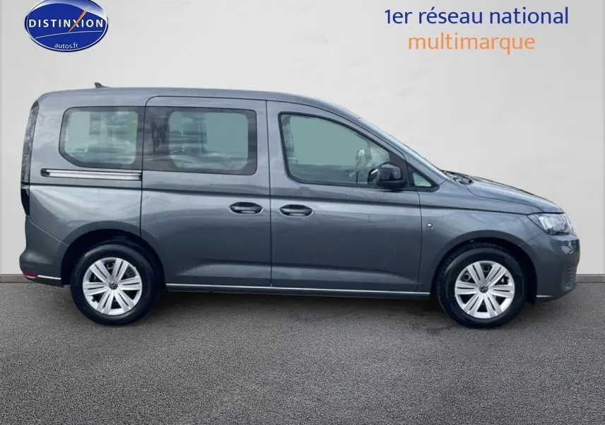 Vue de profil côté gauche d'un Volkswagen Caddy gris indien 2025 sur fond neutre, avec jantes alliage visibles.