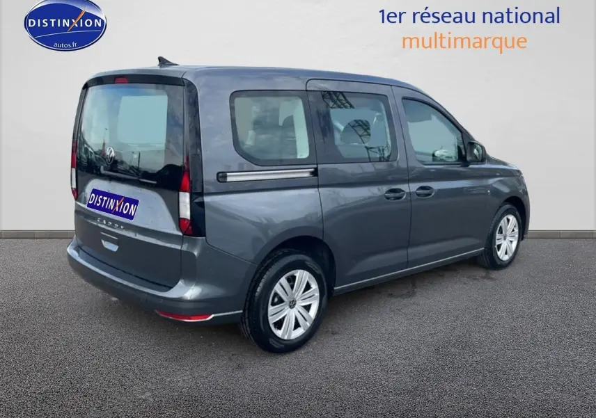 Vue 3/4 arrière droite d'un Volkswagen Caddy gris indien 2025 avec barres de toit et vitres teintées.