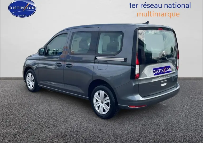 Vue 3/4 arrière droite d'un Volkswagen Caddy gris indien 2025 avec vitres teintées et barres de toit.