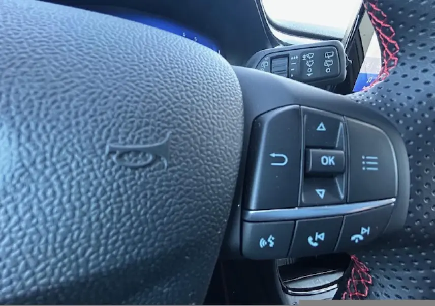 Gros plan sur le volant cuir perforé avec surpiqûres rouges du Ford Puma gris Magnetic, boutons de commande intégrés visibles.