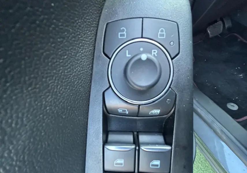 Gros plan sur les commandes de réglage des rétroviseurs et vitres côté conducteur d’un Ford Puma gris Magnetic.