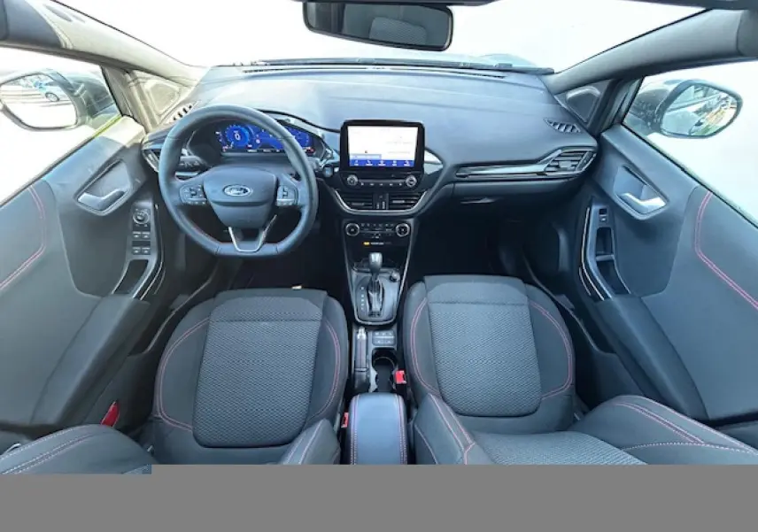 Vue intérieure avant du Ford Puma gris Magnetic 2023, volant ST-Line à méplat avec surpiqûres rouges et écran tactile central.