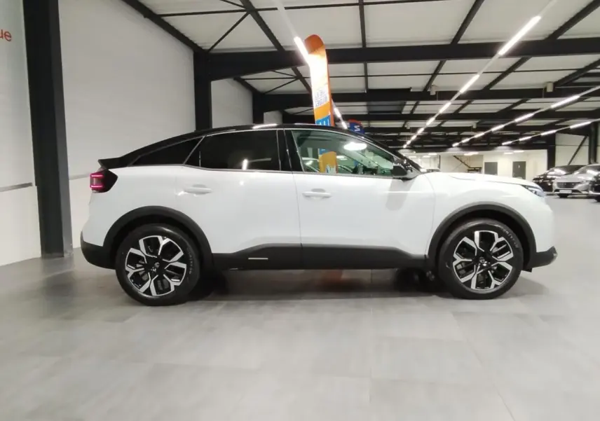 Vue latérale droite d'une Citroën C4 blanche Okenite avec toit noir et jantes alliage 18 pouces en intérieur showroom.