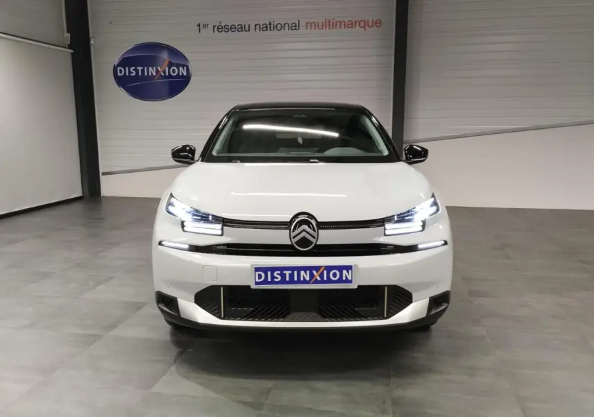 Vue avant d'une Citroën C4 blanche Okenite avec toit noir, feux LED allumés, en intérieur showroom.