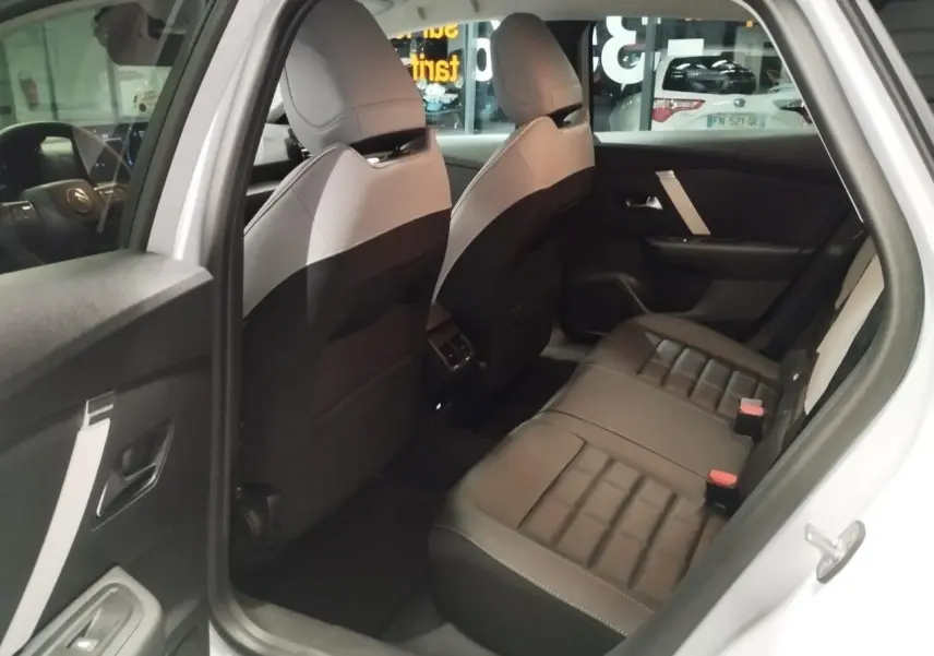 Vue intérieure arrière côté gauche de la Citroën C4 2025 hybride, sièges en cuir noir et gris avec détails blancs.