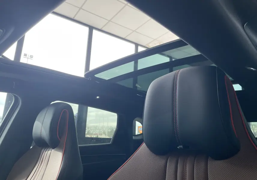 Vue intérieure sur les sièges avant noirs et marron avec surpiqûres rouges, sous un toit ouvrant panoramique vitré.