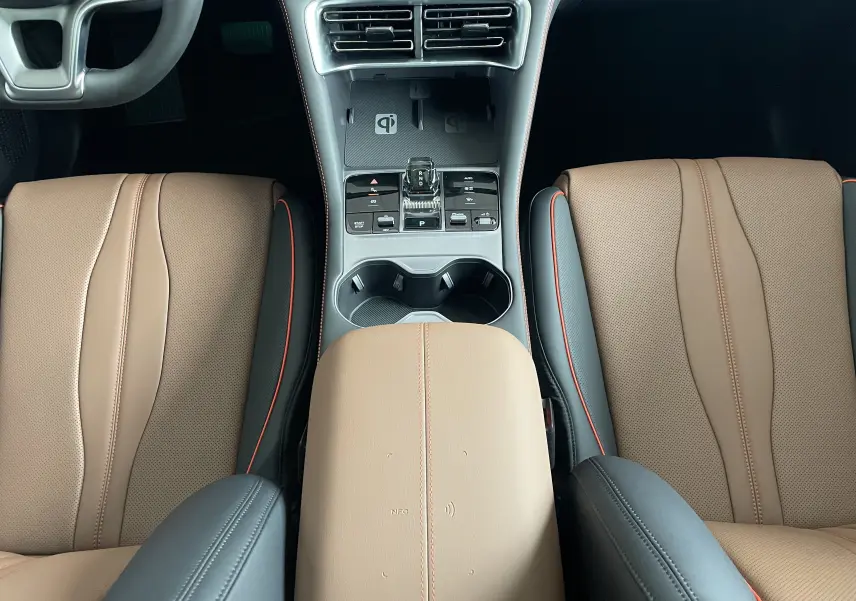 Vue plongeante sur la console centrale et les sièges avant en similicuir brun et noir avec surpiqûres orange du BYD SEAL U 2025.