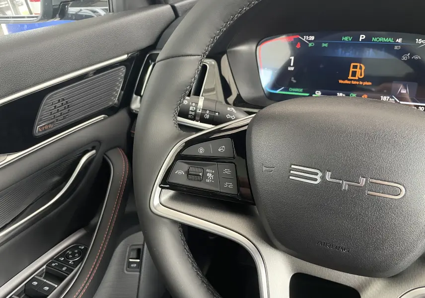 Gros plan sur le volant multifonction et le tableau de bord numérique du BYD SEAL U 2025, intérieur noir avec surpiqûres rouges.