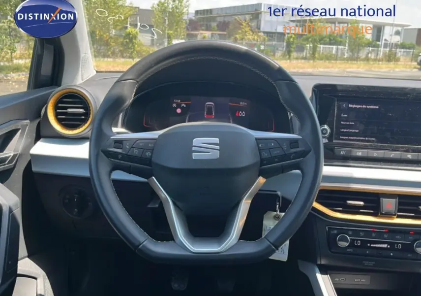 Vue intérieure centrée sur le volant cuir et tableau de bord du SEAT Arona gris avec détails dorés autour des aérateurs.
