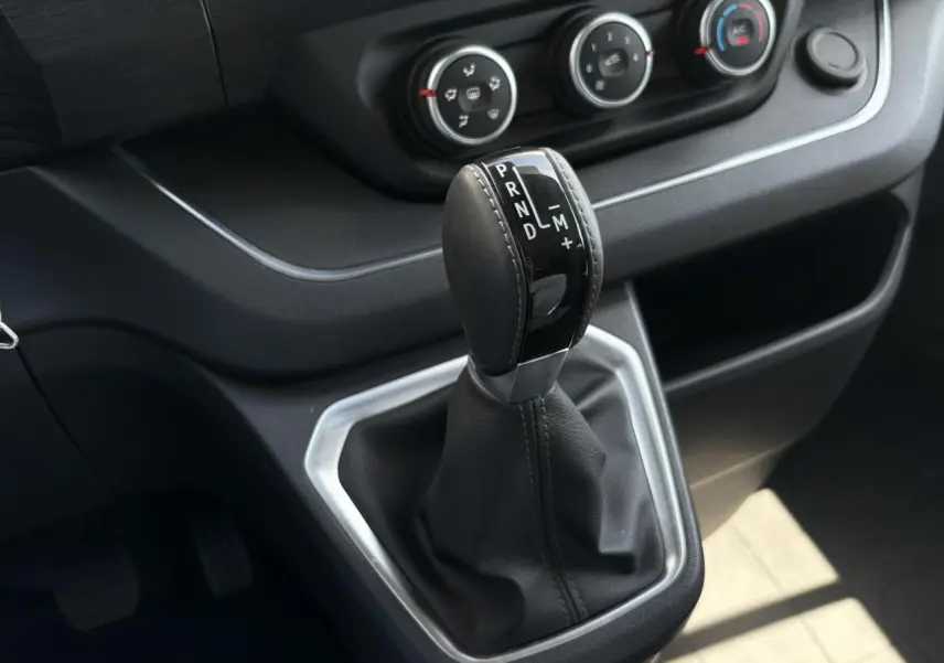Gros plan sur le levier de vitesses automatique noir et argenté du Renault Trafic Fourgon 2024, avec commandes de climatisation visibles.