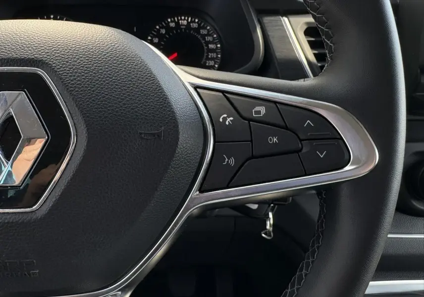 Gros plan sur le volant noir du Renault Trafic Fourgon 2024 avec commandes multifonctions et logo chromé au centre.