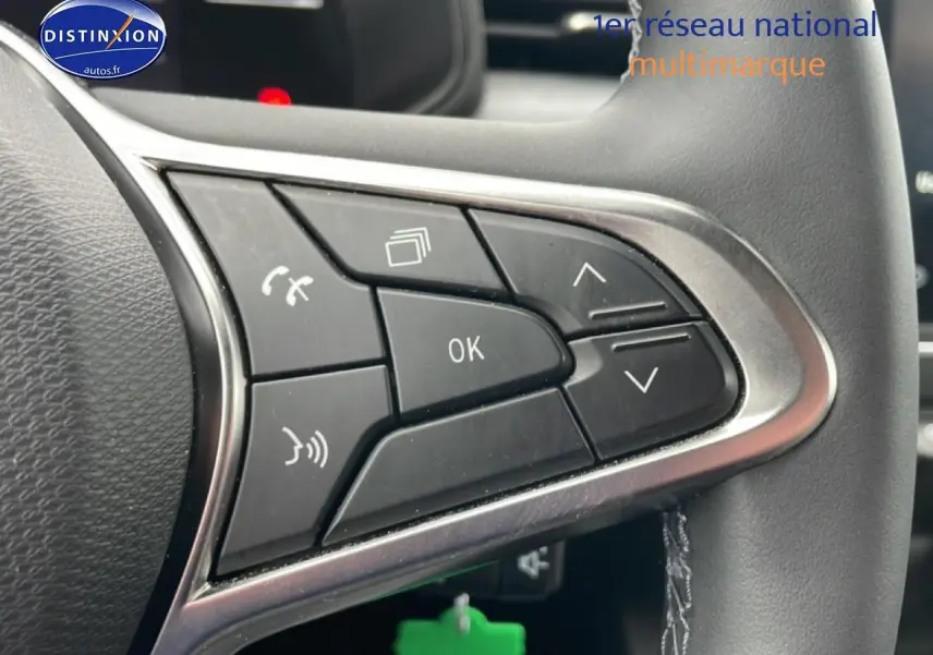 Gros plan sur les commandes multifonctions noires du volant côté droit d’une Renault Clio V blanche.