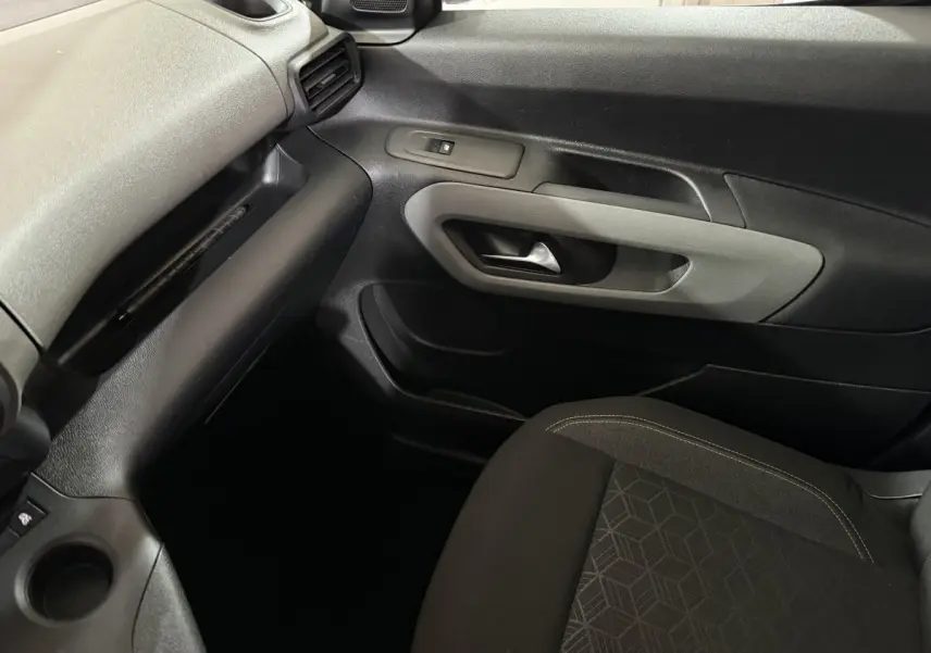 Vue intérieure côté passager du Peugeot Rifter blanc 2019, montrant la porte et le siège tissu noir avec motifs géométriques.