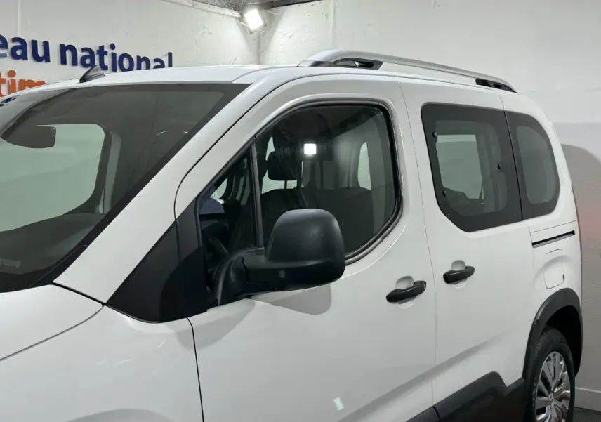 Vue de côté droit avant d'un Peugeot Rifter blanc 2019 avec barres de toit chromées et rétroviseurs noirs.