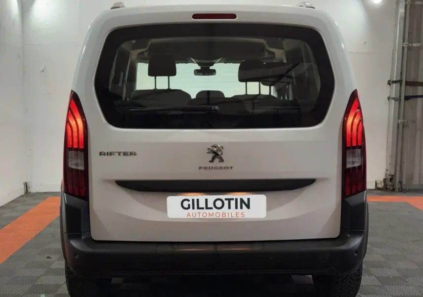 Vue arrière d’un Peugeot Rifter blanc de 2019 avec feux arrière allumés dans un garage.
