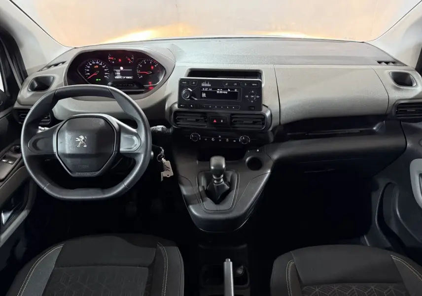 Vue intérieure frontale du tableau de bord noir et gris du Peugeot Rifter avec volant, écran central et levier de vitesses manuel.