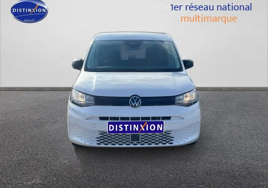 Vue frontale d'un Volkswagen Caddy blanc 2025 avec calandre noire et plaque Distinxion visible.