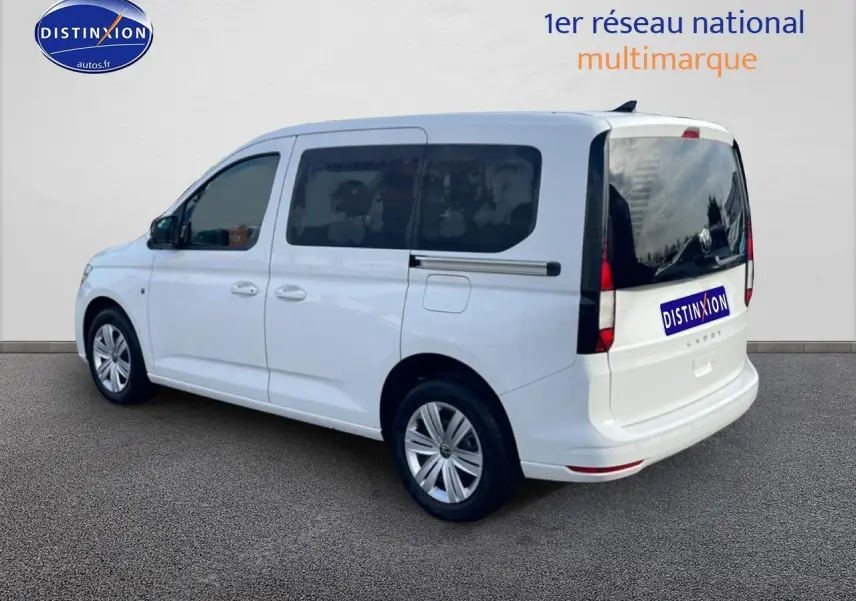 Vue 3/4 arrière droite du Volkswagen Caddy blanc 2025 avec vitres arrière teintées et barres de toit noires.