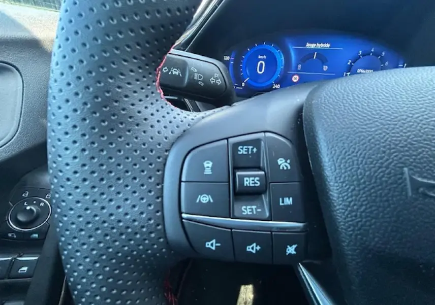 Gros plan sur le volant perforé avec surpiqûres rouges et le combiné numérique bleu du Ford Puma gris Solar 2023.