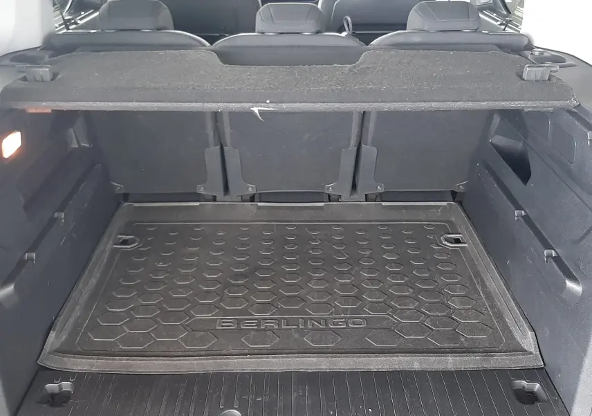 Vue du coffre ouvert d'un Citroën Berlingo 2019 vert, avec tapis de coffre marqué "BERLINGO" et sièges arrière visibles.