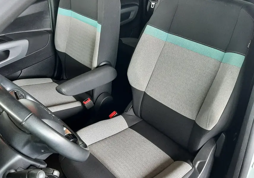 Vue intérieure côté conducteur du Citroën Berlingo 2019, sièges tissu gris clair avec bande turquoise et accoudoir.