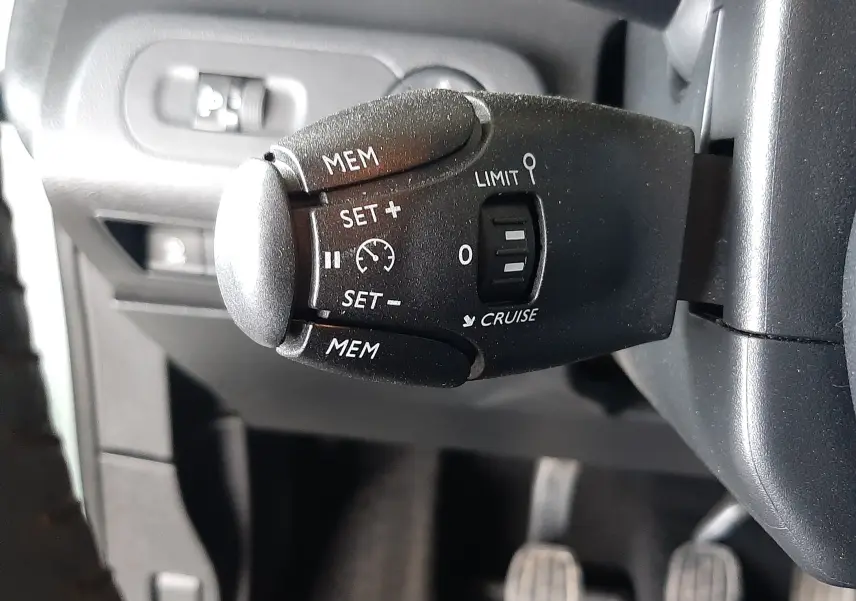 Gros plan sur la commande de régulateur de vitesse noire à gauche du volant dans l’habitacle gris du Citroën Berlingo vert 2019.