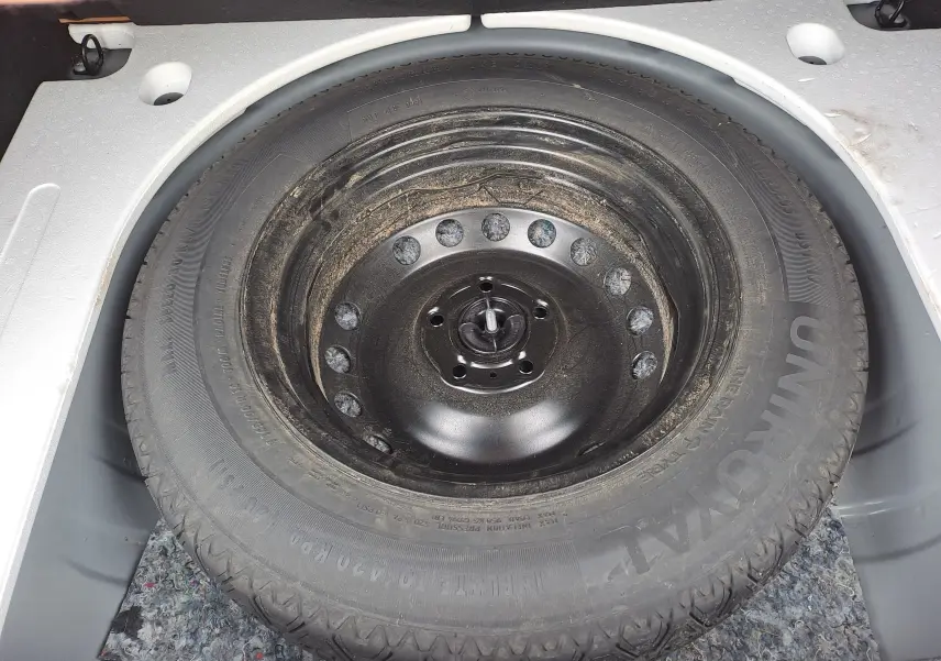 Roue de secours noire dans le coffre d'un Dacia Duster gris urbain, vue en plongée sur le pneu.