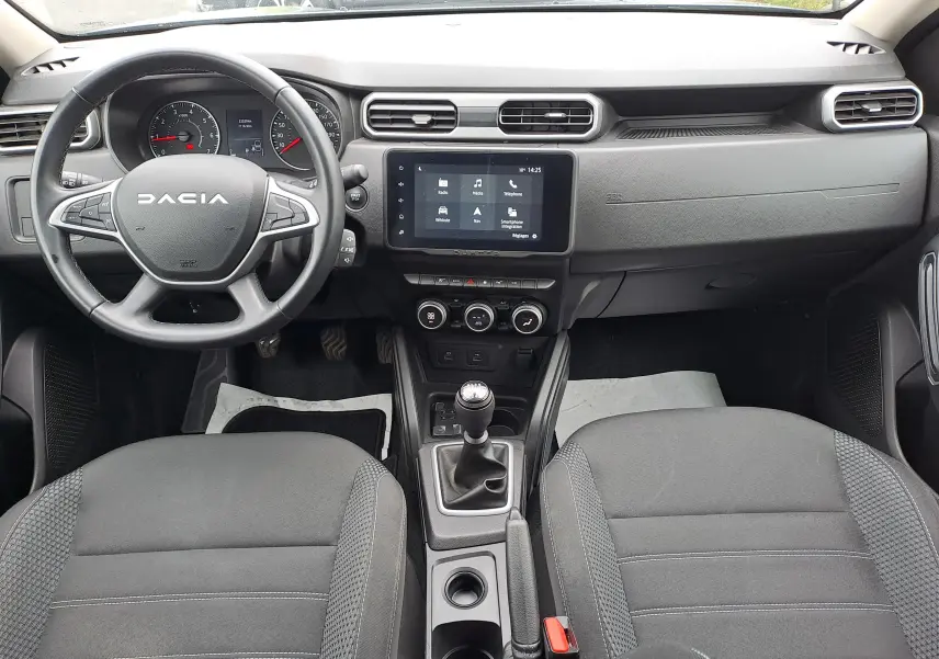 Vue intérieure avant du Dacia Duster 2024, tableau de bord noir avec écran tactile et volant multifonction.