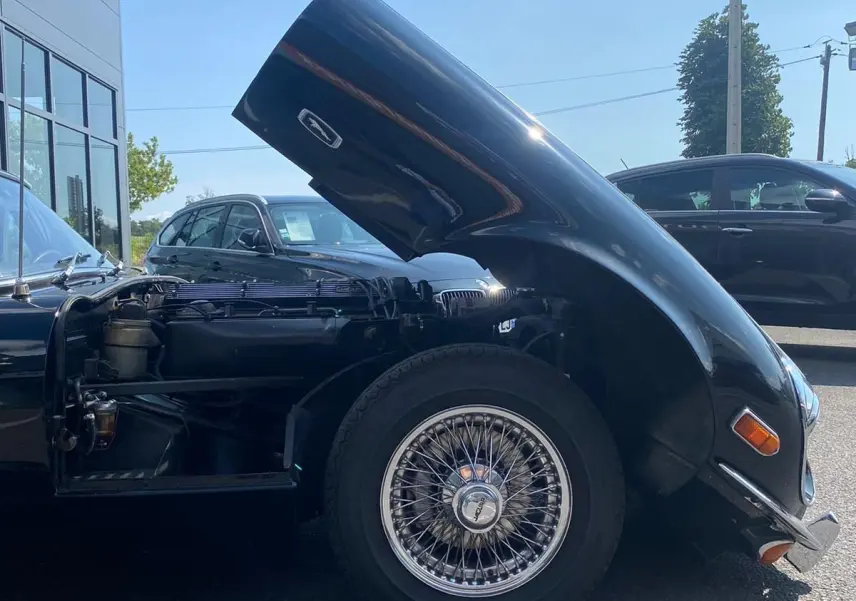 Vue latérale gauche d'une Jaguar S-Type noire de 1970 avec capot avant relevé et roue à rayons visible.