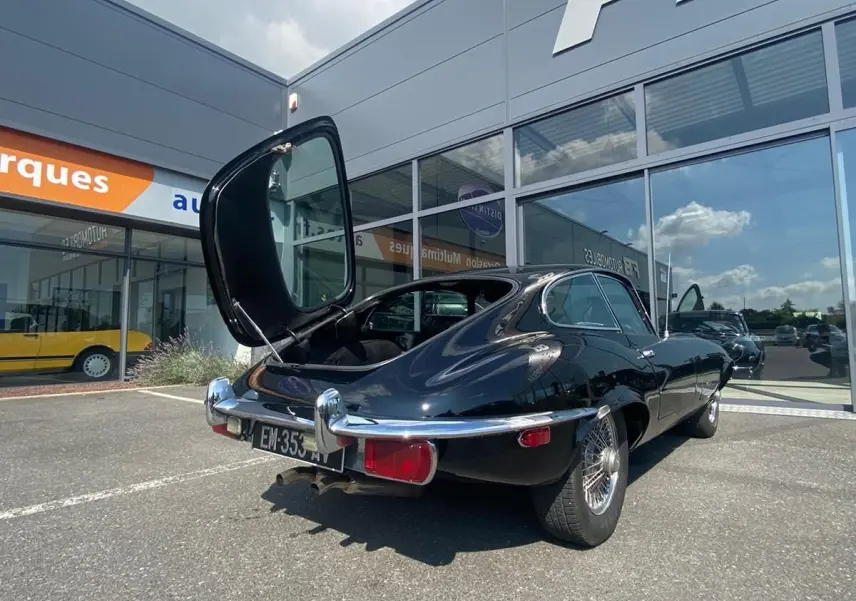 Vue 3/4 arrière gauche d'une Jaguar S-Type noire de 1970 avec coffre ouvert, garée devant un bâtiment moderne.