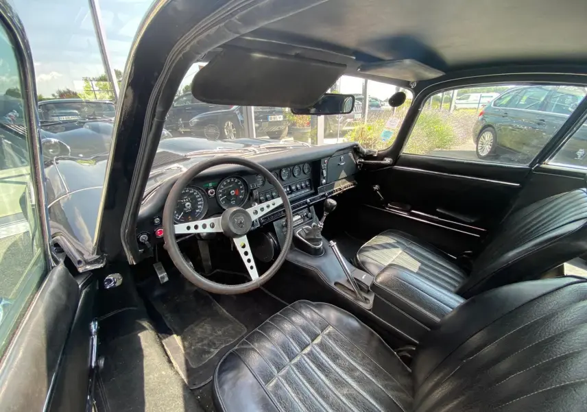 Vue intérieure côté conducteur de la Jaguar S-Type noire de 1970, avec tableau de bord vintage et boîte manuelle.