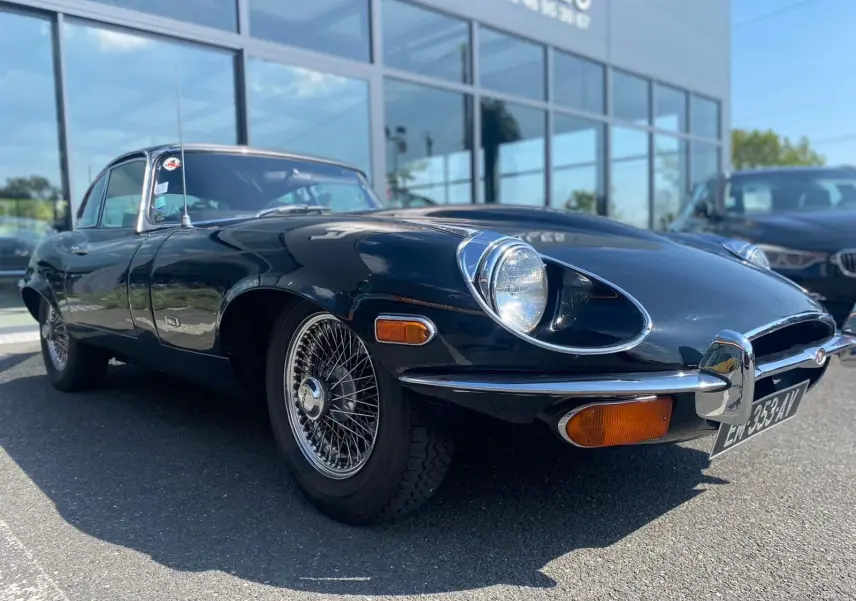 Jaguar Type E Coupé noir vue 3/4 avant droit, mettant en valeur ses phares ovales et jantes à rayons chromés.