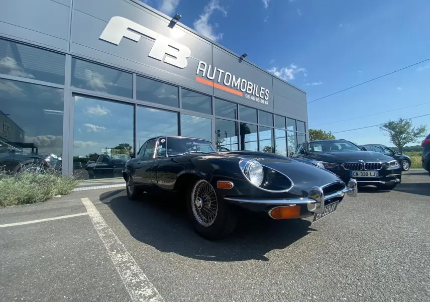 Jaguar Type E Coupé noir 1970 vue 3/4 avant droit, avec jantes à rayons et phares ronds caractéristiques.