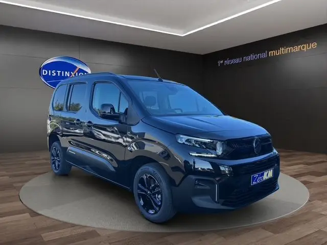 Vue 3/4 avant du Citroën Berlingo N1 BlueHDi 130 noir avec jantes noires et caméra, en intérieur showroom.