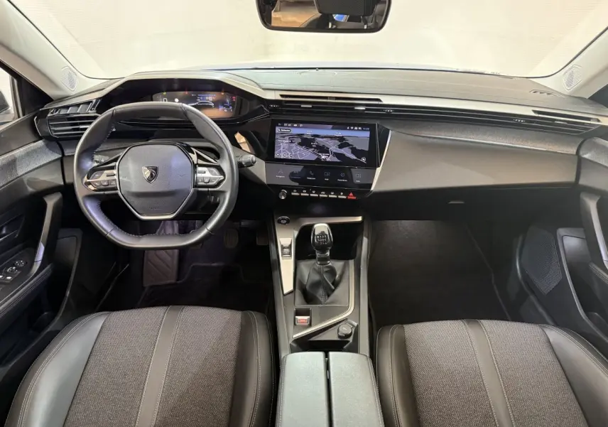 Vue intérieure avant de la Peugeot 308 2023, tableau de bord noir avec écran tactile central et volant cuir multifonctions.