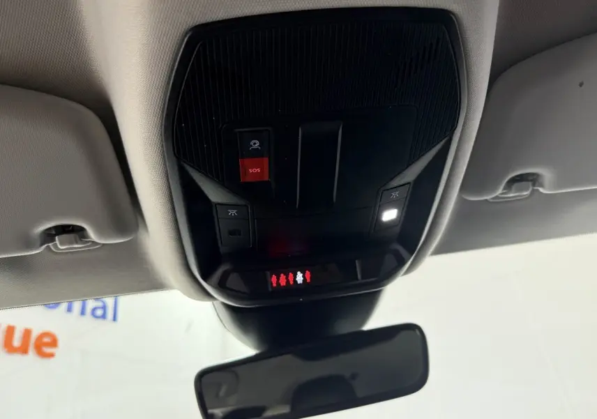 Vue intérieure en plongée du panneau de commandes au plafond noir avec bouton SOS rouge et éclairage dans une Peugeot 308 bleu 2023.