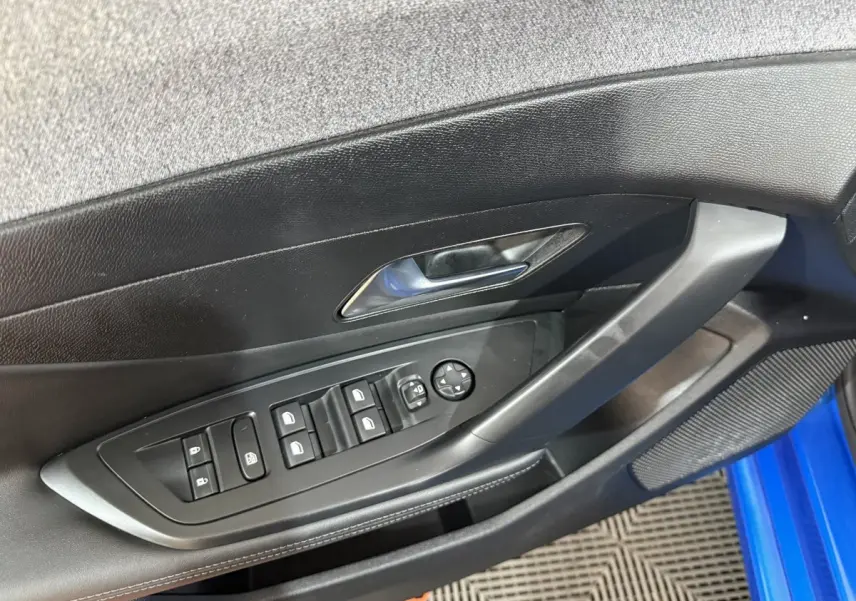 Vue rapprochée de la porte côté conducteur d’une Peugeot 308 bleu 2023, avec commandes des vitres et rétroviseurs.