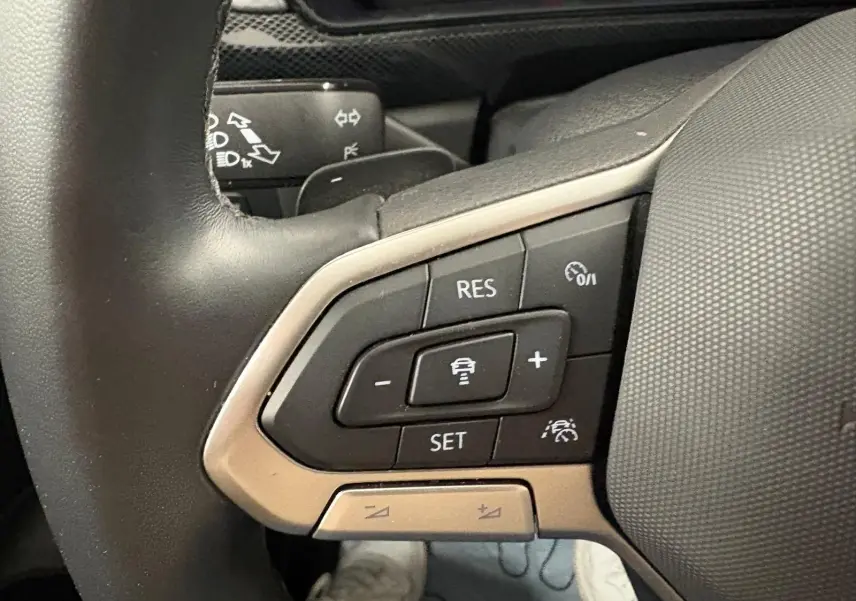 Gros plan sur les commandes du régulateur de vitesse au volant cuir du Volkswagen T-Cross 2024 couleur reflet d'argent.