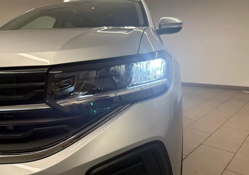 Gros plan sur le phare avant droit allumé d'un Volkswagen T-Cross 2024 couleur reflet d'argent, intérieur showroom.