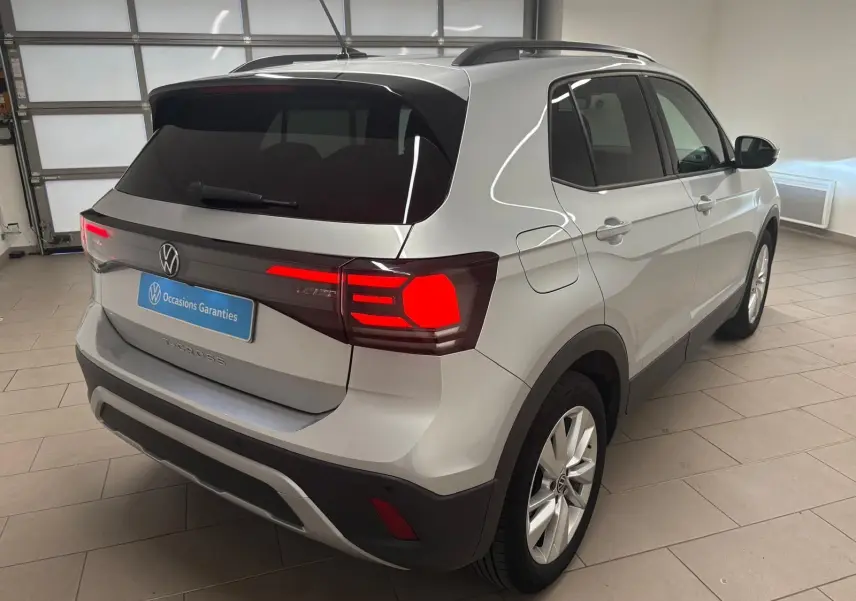 Vue 3/4 arrière droite du Volkswagen T-Cross 2024 en reflet d'argent avec feux arrière allumés dans un garage.
