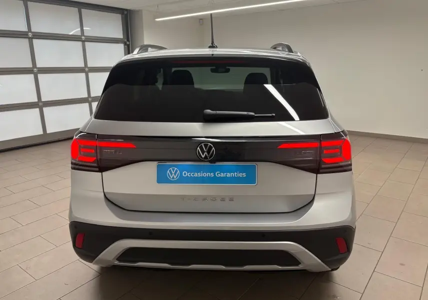 Vue arrière d'un Volkswagen T-Cross 2024 couleur reflet d'argent avec feux arrière LED allumés en intérieur.