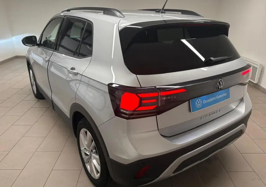 Vue 3/4 arrière droite du Volkswagen T-Cross 2024 en reflet d'argent avec feux arrière LED allumés et vitres surteintées.