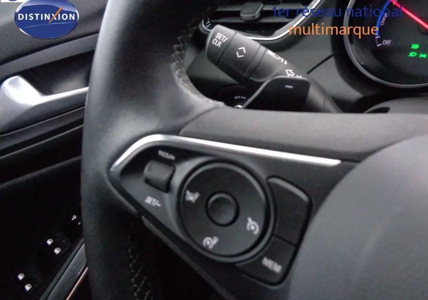 Gros plan sur le volant noir de l'Opel Grandland X hybride, montrant les commandes intégrées et le tableau de bord partiel.