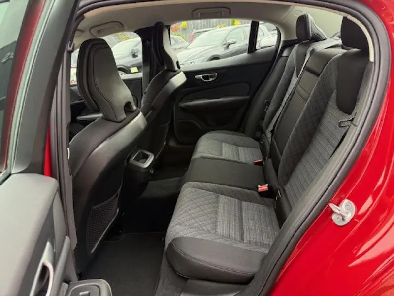Vue intérieure arrière côté gauche du Volvo S60 2024 Rouge Fusion Métallisé, sièges tissu gris et noir avec appuie-têtes intégrés.
