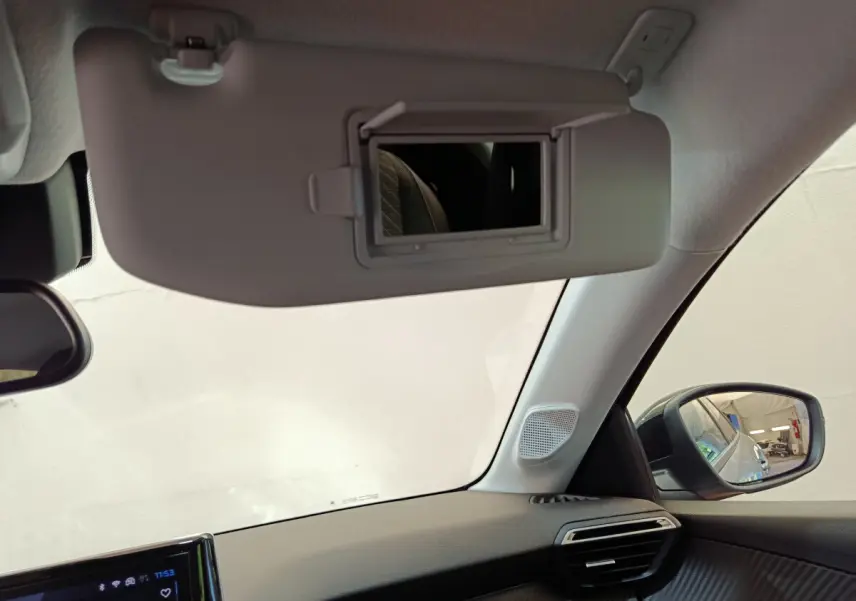 Intérieur côté conducteur du Peugeot 208 gris clair, avec pare-soleil ouvert et rétroviseur extérieur visible.