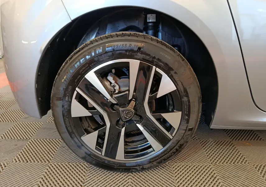 Gros plan sur la roue avant droite gris clair de la Peugeot 208 PureTech 100 S&S Allure avec jante noire et argentée.