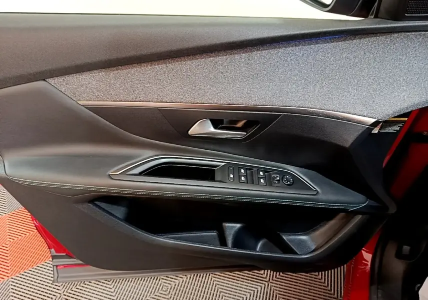 Vue intérieure côté gauche de la porte avant rouge du Peugeot 3008 avec commandes de vitres et poignée argentée.