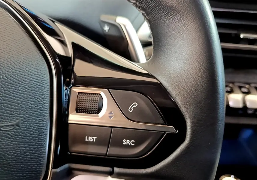 Gros plan sur les commandes gauche du volant cuir noir du Peugeot 3008 hybride, avec molette et boutons fonctionnels.